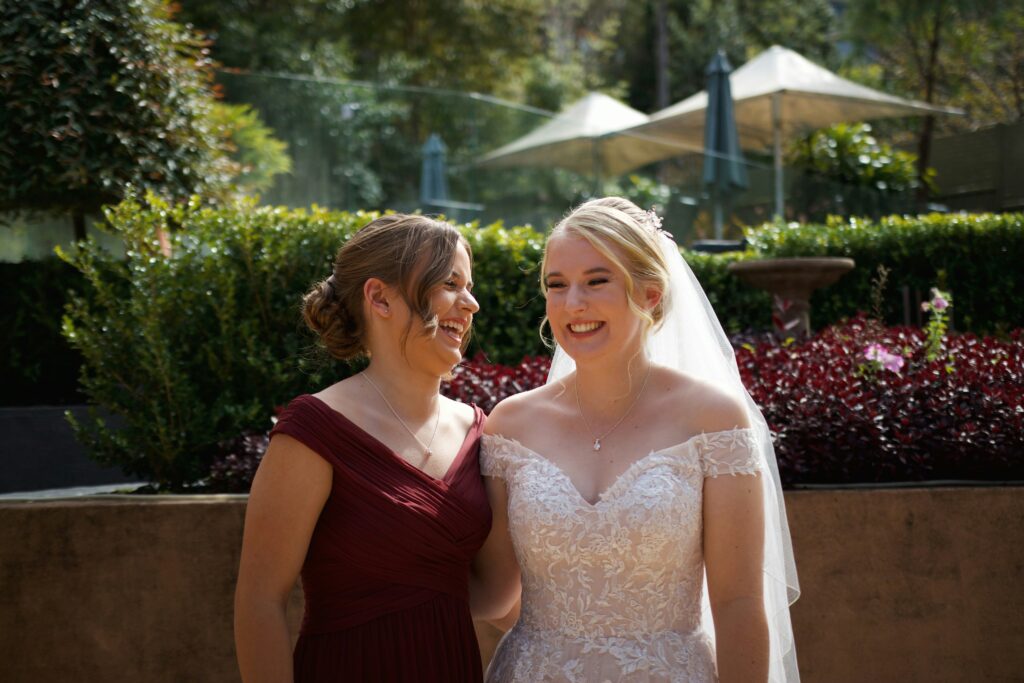 A smiling bride hugging her sister, the maid of honor, on her wedding day. "alt text: A heartwarming moment between sisters on a bride's special day