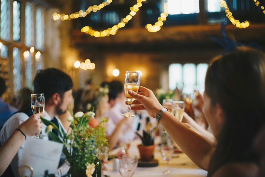 A best man raising a glass in a toast, with the bride and groom smiling in the background.
